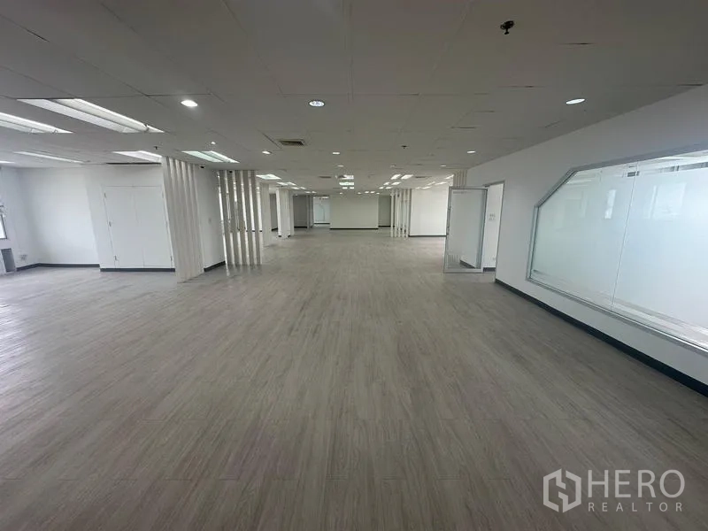 Office Space for rent - Long open-plan office with internal glass panels, pale vinyl flooring, and multiple ceiling light trays.
