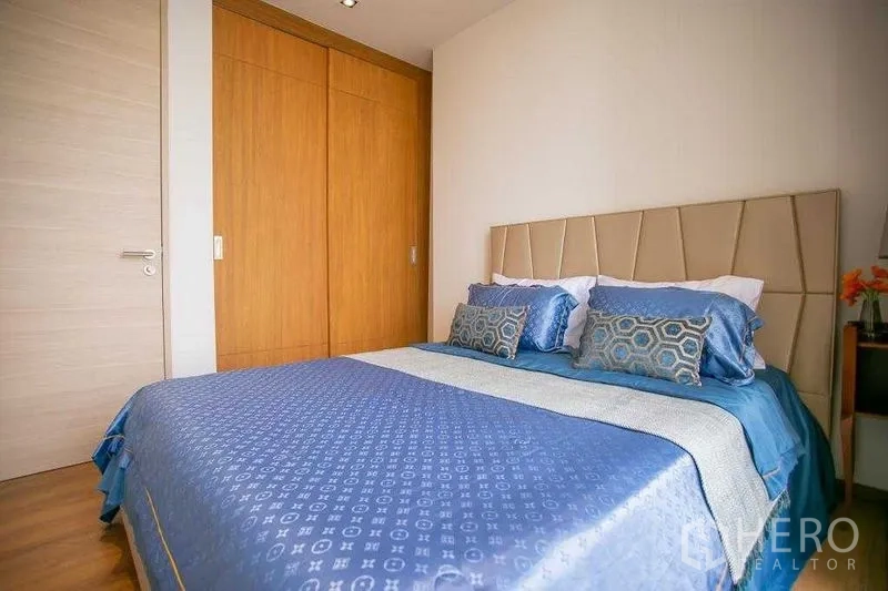 Condominium for sale in Khlong Toei, Bangkok - Bedroom angle showing built-in wooden wardrobe and upholstered headboard.