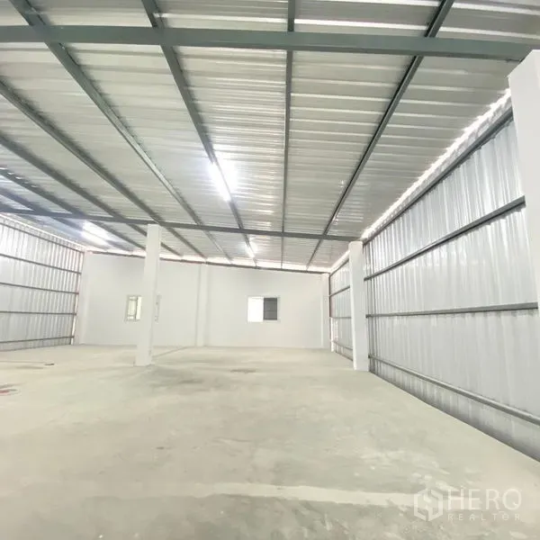 Warehouse for rent in Bang Khae, Bangkok - Bright warehouse interior showing metal roof beams, LED lighting, concrete floor and support columns.