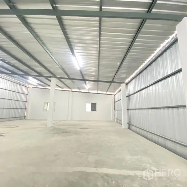 Warehouse for rent in Bang Khae, Bangkok - Bright warehouse interior showing metal roof beams, LED lighting, concrete floor and support columns.