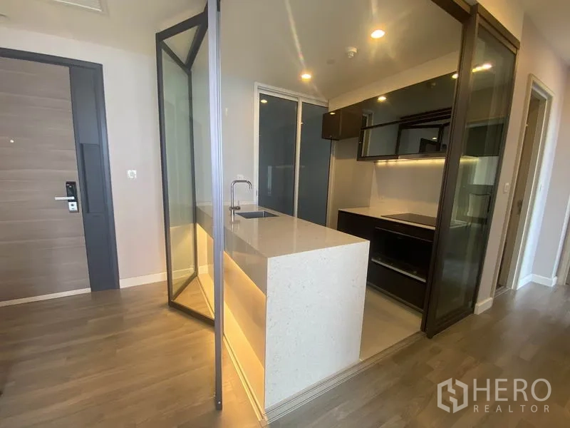 Condominium for rent in Bang Rak, Bangkok - Entryway view to the kitchen with illuminated island and glass partition.