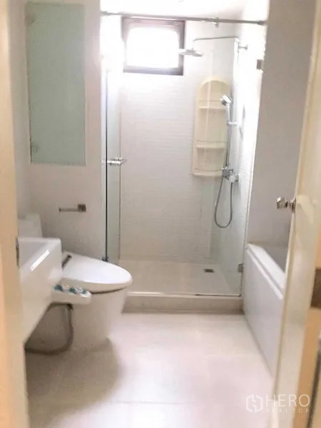 Condominium for rent in Khlong Toei, Bangkok - Bright bathroom with glass-enclosed shower, bathtub, and small window in a modern condo.