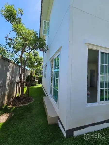 Detached House for rent in Thanyaburi, Pathum Thani - Narrow lawn along the side of the house with trees and wide sliding windows.