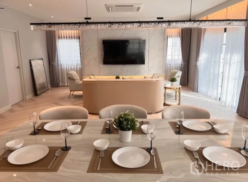 独栋房屋 for rent in Bang Phli, Samut Prakan - 餐桌特写，餐具摆设整齐，视线延伸至电视墙与弧形沙发。