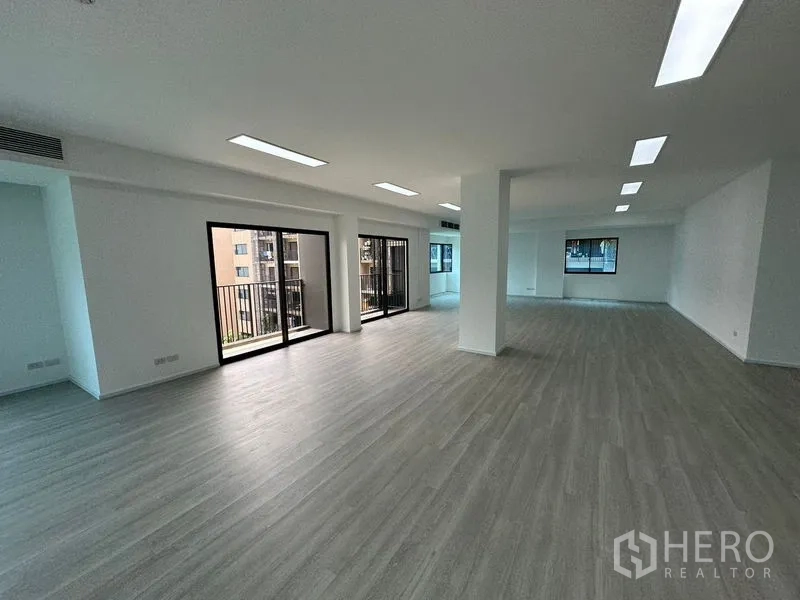 办公空间 出租 - 明亮的办公室内景，双扇推拉门、阳台栏杆、中央立柱与长条嵌入式照明。