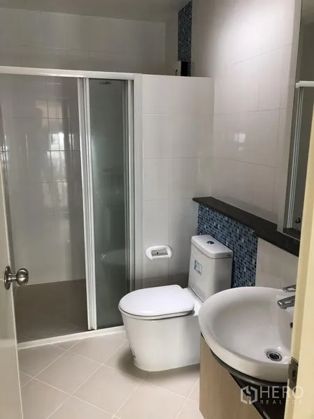 Townhouse for rent in Prawet, Bangkok - Modern bathroom with glass-enclosed shower, vanity and toilet with mosaic accents.