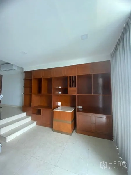 Condominium for rent in Sathon, Bangkok - Living area with floor-to-ceiling built-in wooden shelving and cabinets beside wide windows.