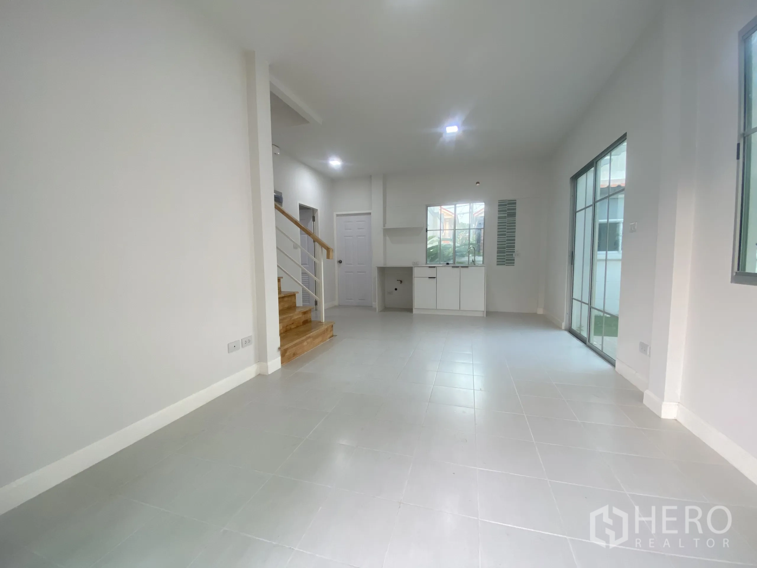 บ้าน ขายในNonthaburi - พื้นที่นั่งเล่นรับประทานอาหารกว้าง ปูกระเบื้อง บันได และประตูกระจกออกสู่สวน.