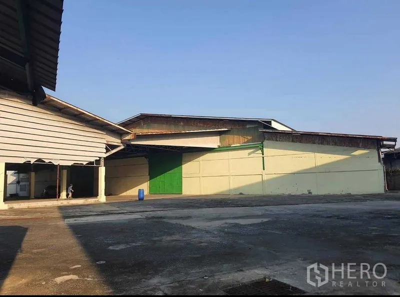 Warehouse for rent or sale in Mueang Pathum Thani, Pathum Thani - Warehouse exterior with a large green sliding door and open paved circulation space.