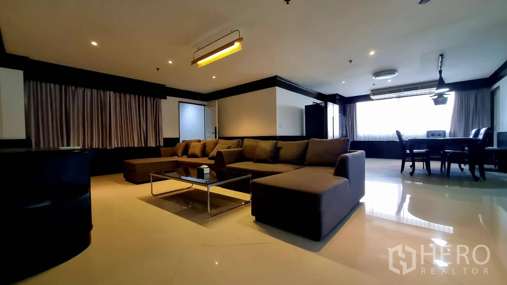 Condominium for rent in Watthana, Bangkok - Open-plan lounge with large L-shaped sofa and dining area by the window.