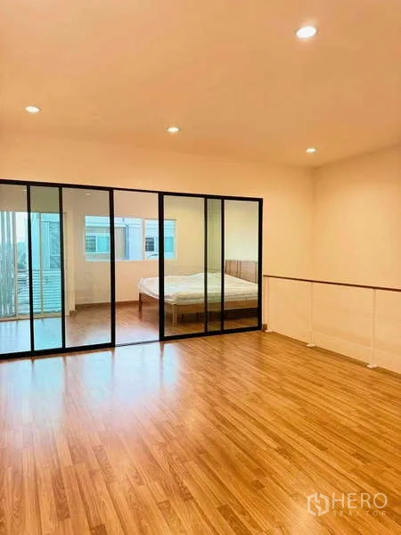 Townhouse for rent in Suan Luang, Bangkok - Spacious master level with wood flooring and full-height glass partition separating the bedroom.