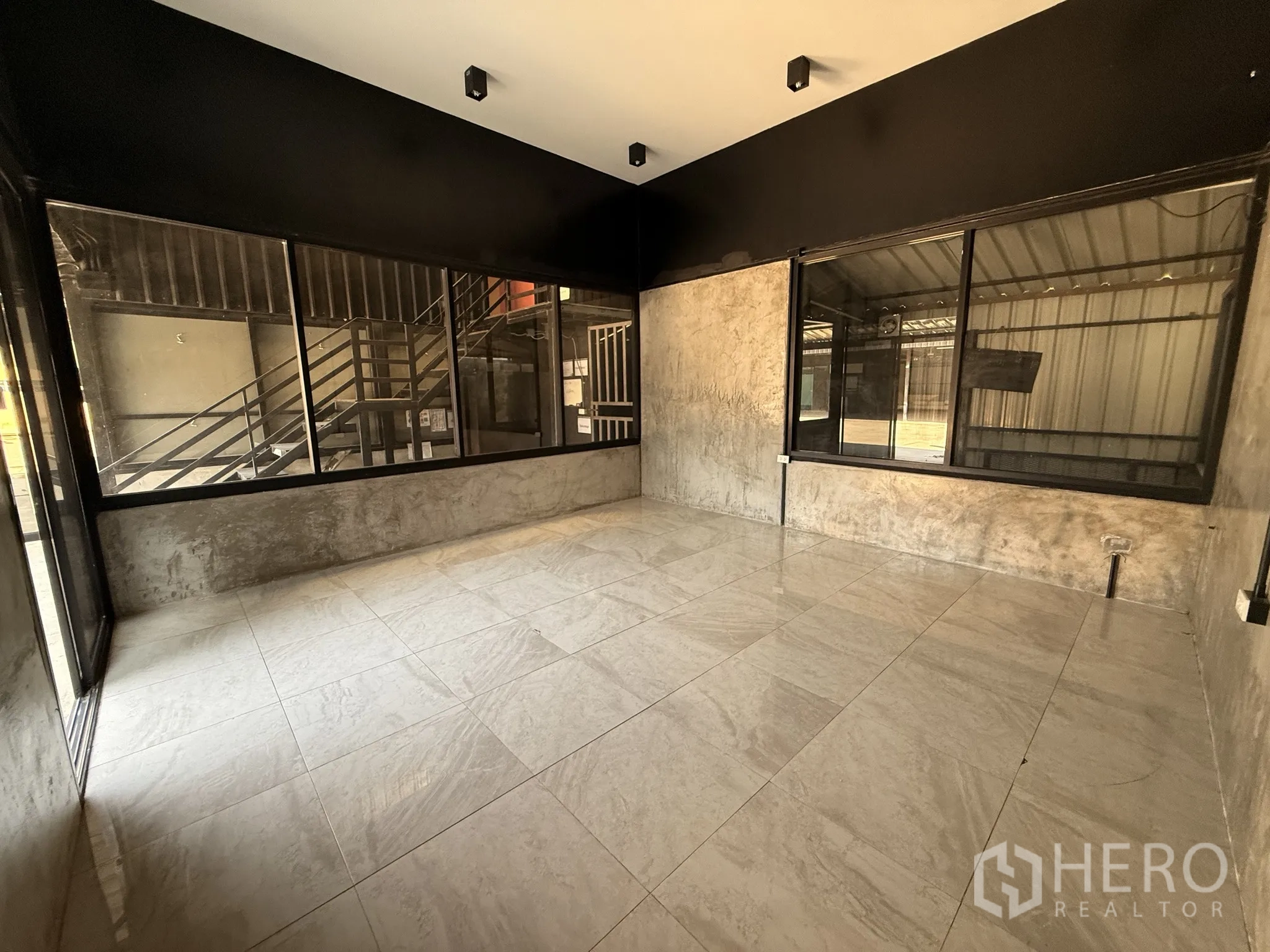 货栈 for rent in Lat Krabang, Bangkok - 一层办公室，浅色地砖与大窗户，可见外部金属楼梯。