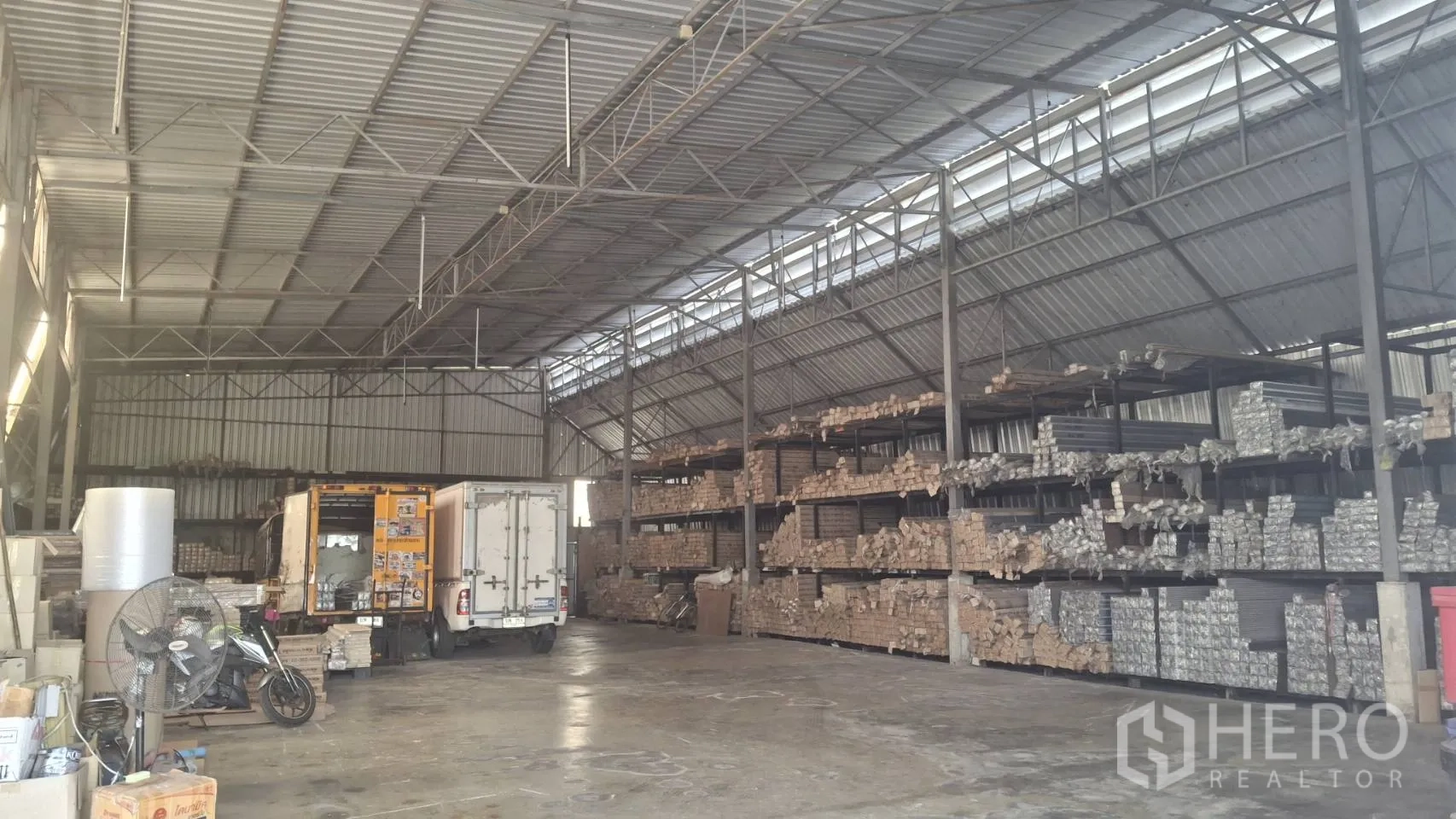 Warehouse for sale in Lam Luk Ka, Pathum Thani - Spacious warehouse interior with high steel truss roof, concrete floor, wide truck loading area and long rows of heavy-duty storage racks.