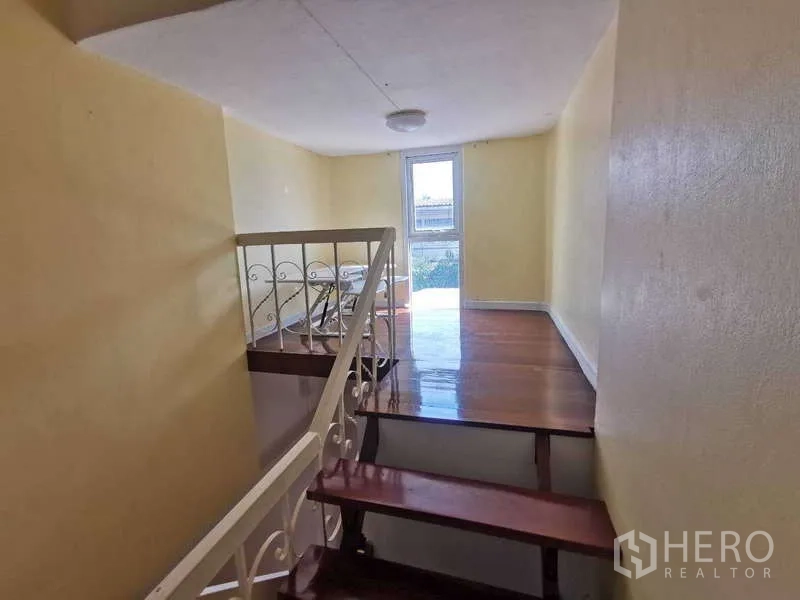 Townhouse for rent in Chatuchak, Bangkok - Staircase landing with wooden steps and daylight through a rear door.