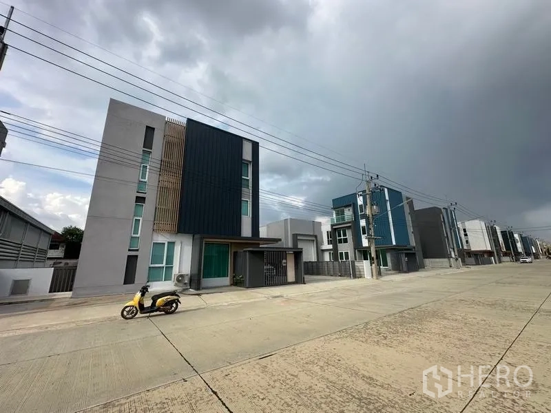 Warehouse for sale in Pathum Thani - Row of contemporary warehouses along a wide concrete street under cloudy skies in Lam Luk Ka.