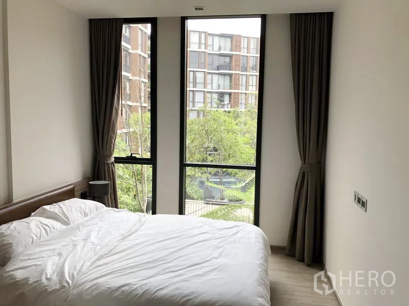 Condominium for rent in Watthana, Bangkok - Cozy bedroom with large windows overlooking landscaped courtyard greenery.