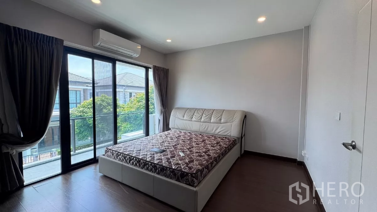 Detached House for rent or sale in Saphan Sung, Bangkok - Primary bedroom with sliding glass doors to a balcony, air conditioner and leafy neighborhood view.