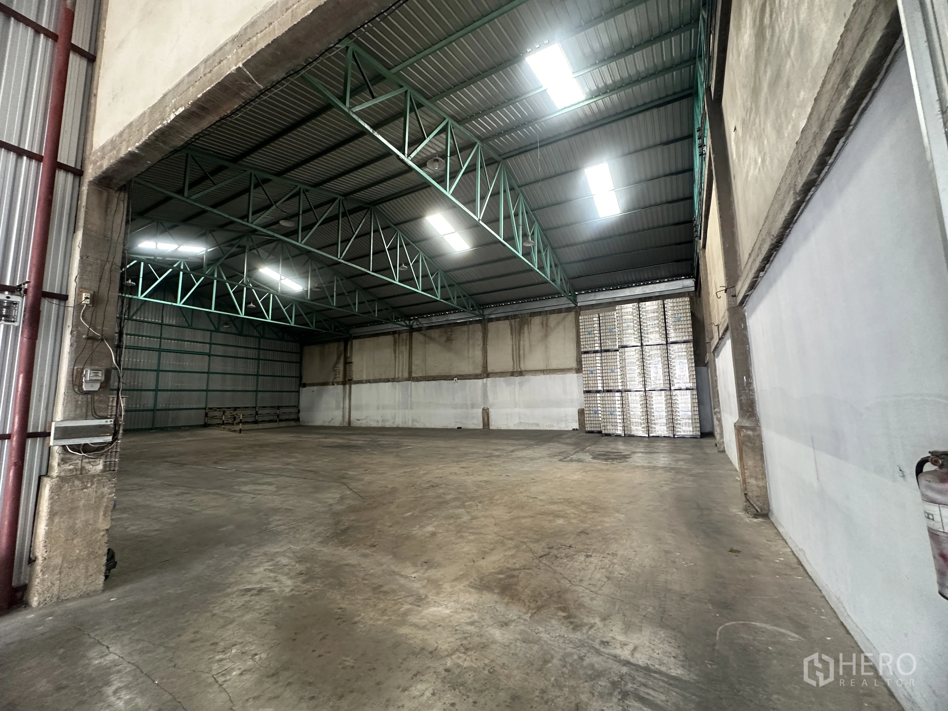 Warehouse for rent in Mueang Pathum Thani, Pathum Thani - Open storage area viewed from the entry with metal wall panels and reinforced concrete floor.