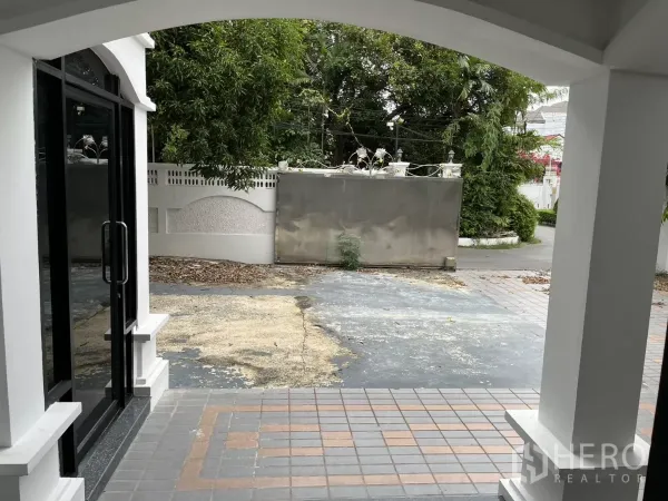 Detached House for rent in Watthana, Bangkok - View from the covered porch to the gated driveway with a tiled forecourt and mature trees.