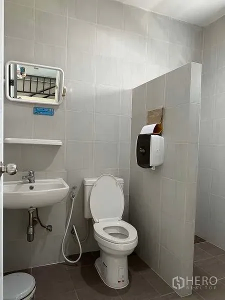 Factory for rent in Samut Prakan - Clean tiled restroom with toilet, sink and mirror inside the factory.