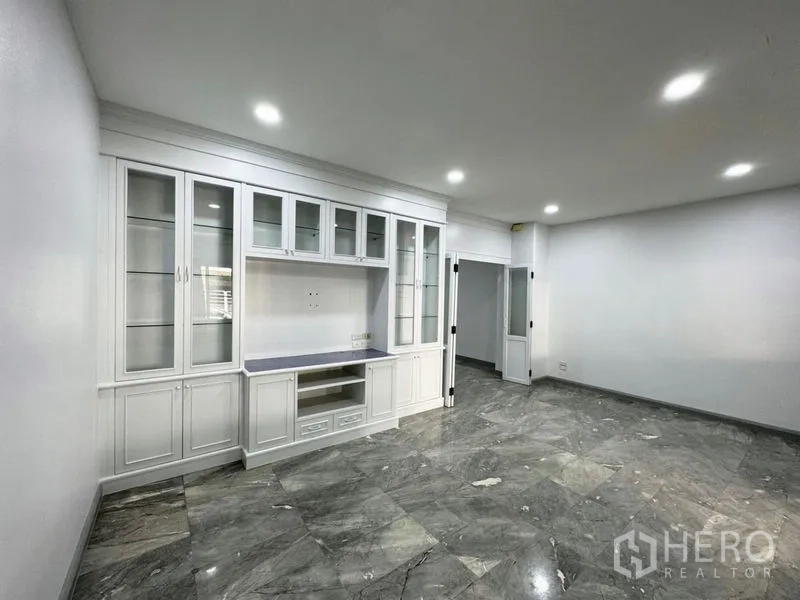 Townhouse for rent or sale in Suan Luang, Bangkok - Living area with white built-in display unit and downlights on stone tiles