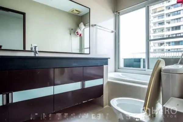Condominium for rent or sale in Watthana, Bangkok - Bright bathroom with long vanity, bathtub by the window and toilet.