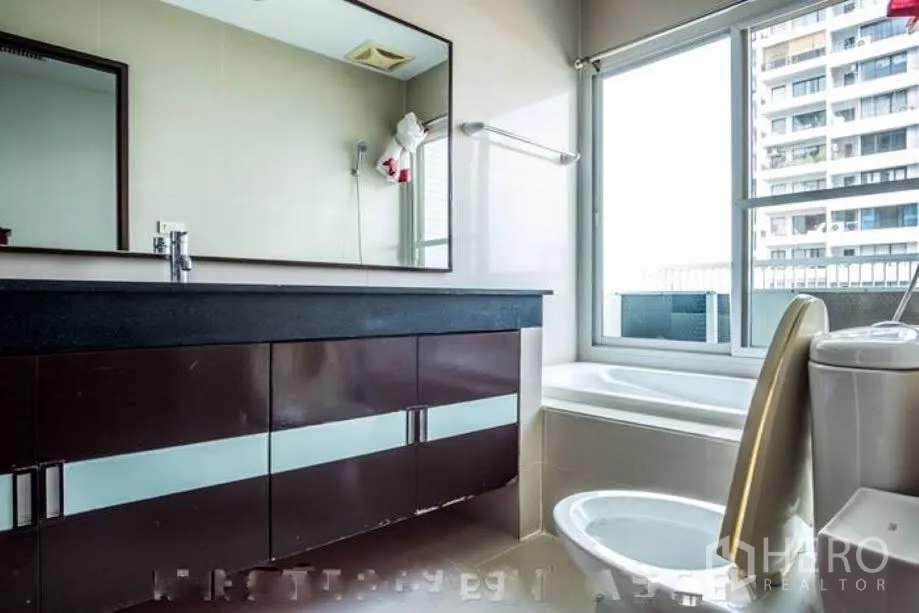Condominium for rent or sale in Watthana, Bangkok - Bright bathroom with long vanity, bathtub by the window and toilet.