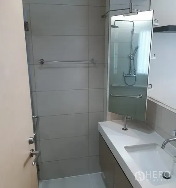 Condominium for rent in Khlong Toei, Bangkok - Contemporary bathroom with glass shower, wall-mounted shower set, vanity with sink, and mirror cabinet.