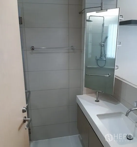 Condominium for rent in Khlong Toei, Bangkok - Contemporary bathroom with glass shower, wall-mounted shower set, vanity with sink, and mirror cabinet.