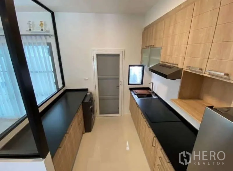 Townhouse for rent in Bang Phli, Samut Prakan - Galley kitchen view with long counters and door to utility area.
