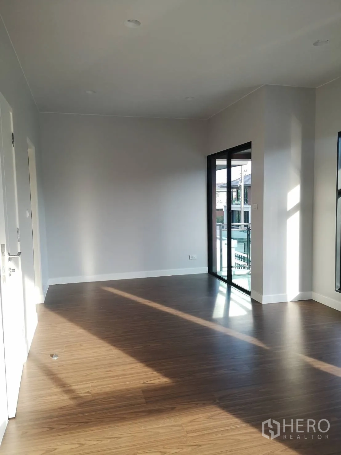 Detached House for sale in Lam Luk Ka, Pathum Thani - Spacious upstairs room with sliding glass door to a balcony and timber flooring.
