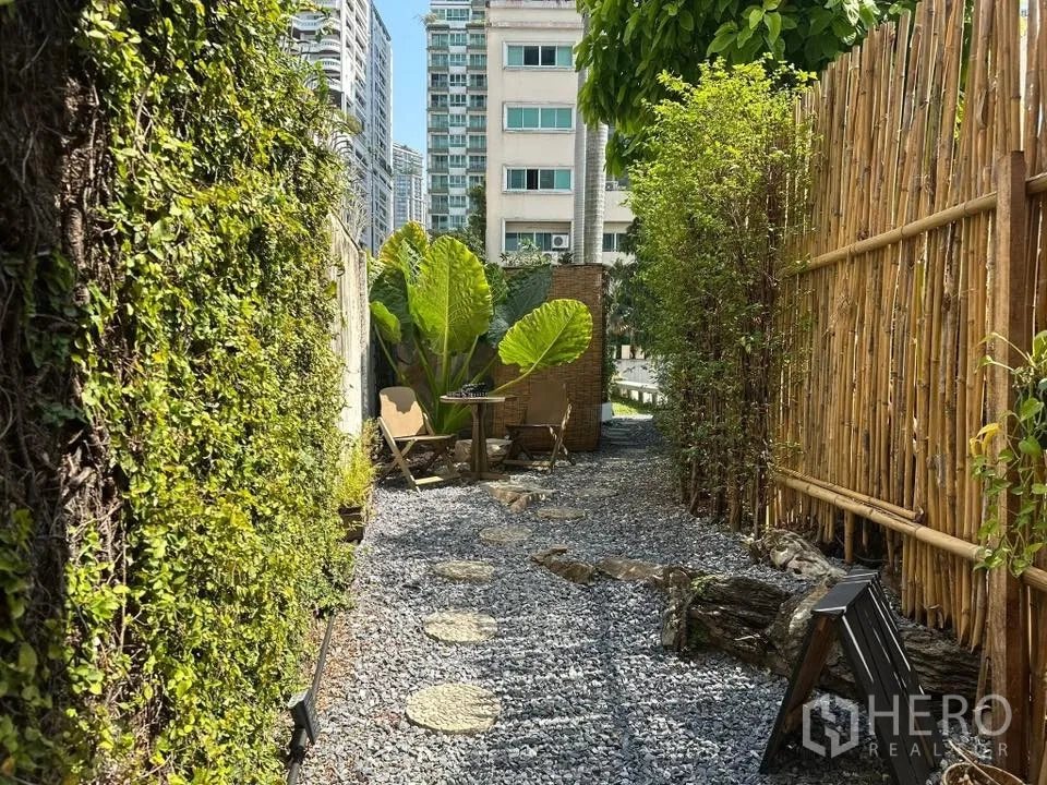 Retail Space for rent in Khlong Toei, Bangkok - Gravel path lined with bamboo and green vines, with plants and city buildings in the background.