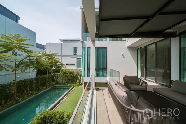 Detached House for rent or sale in Saphan Sung, Bangkok - Balcony seating overlooking a lap pool, trimmed lawn and minimalist neighboring homes.