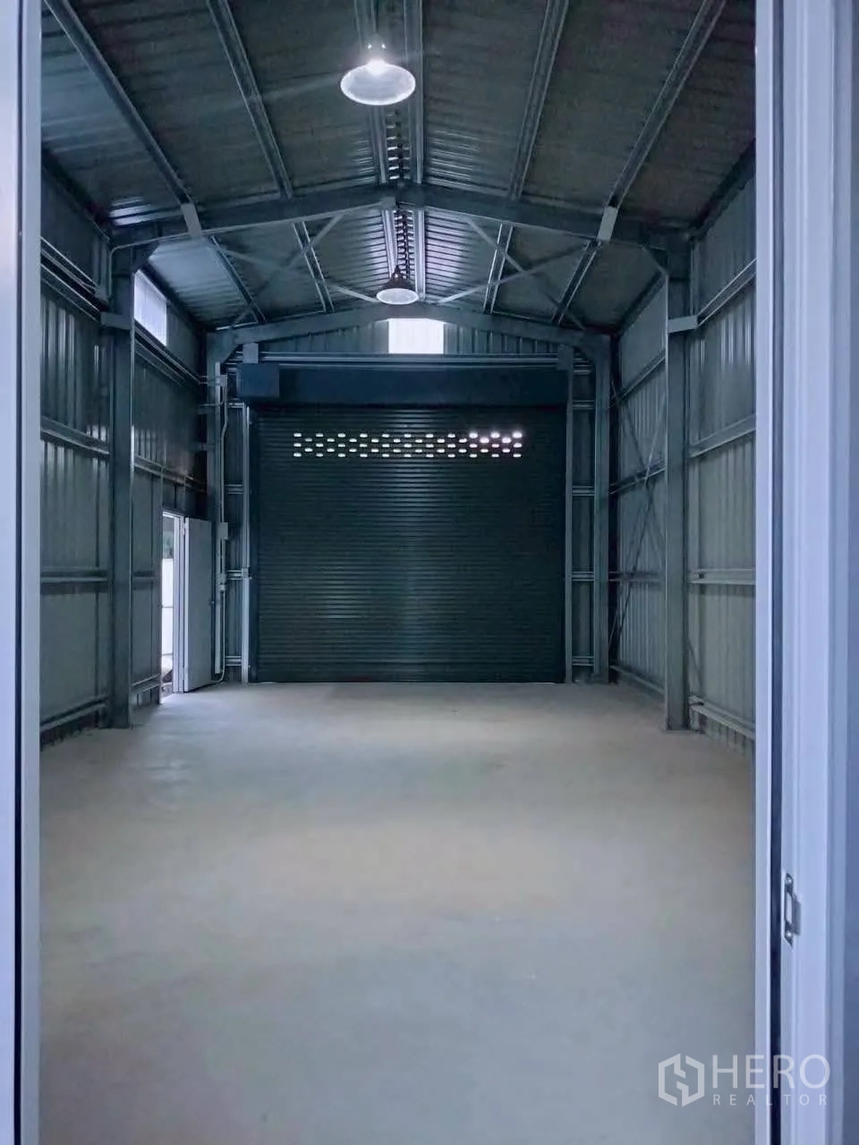 Warehouse for rent in Lat Phrao, Bangkok - Long warehouse interior facing a wide roller shutter door with pendant lights overhead.