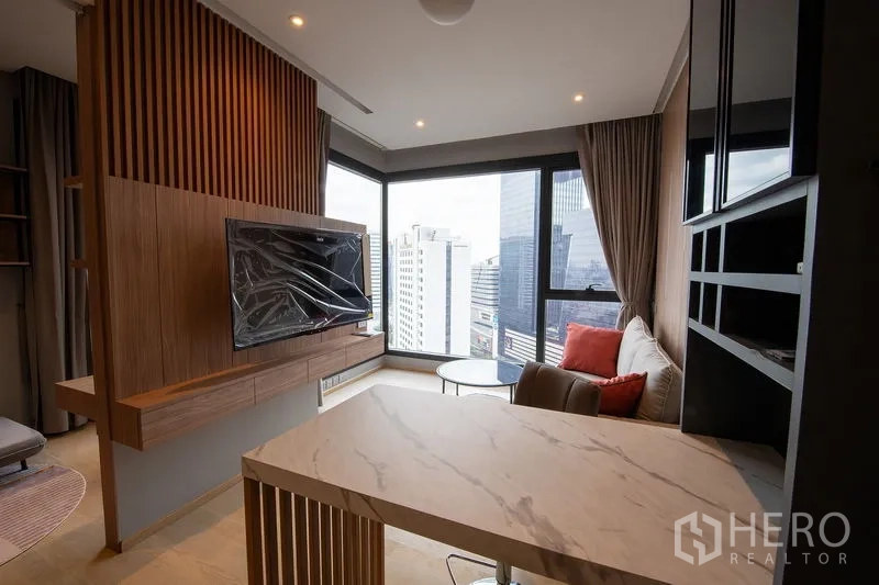 Condominium for rent in Din Daeng, Bangkok - Corner living area with floor-to-ceiling windows, city skyline view, wood feature wall and a marble breakfast bar with mounted TV.