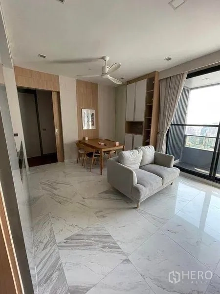 Condominium for rent or sale in Bang Rak, Bangkok - Sunlit living room with sofa, marble flooring, and a balcony facing the city.