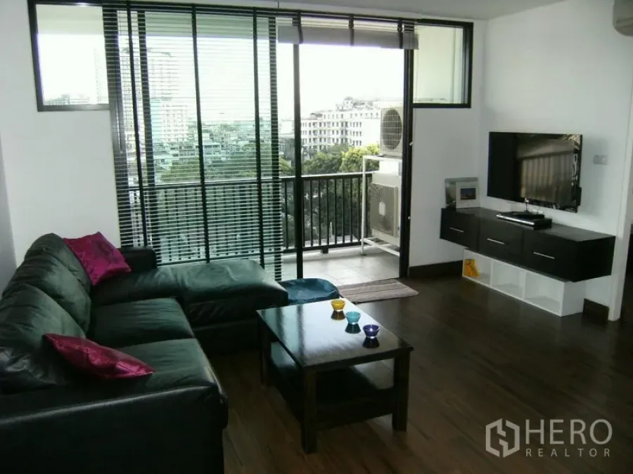公寓 出租在Watthana, Bangkok - 客厅设L形沙发、壁挂电视，通向可观城市景观的阳台。