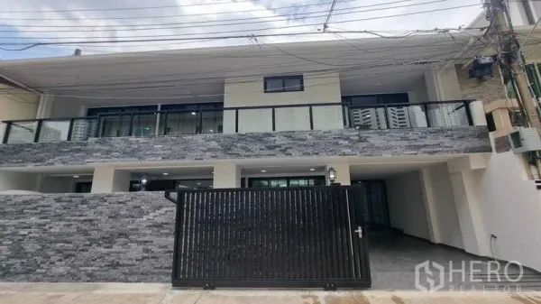 联排别墅 出租在Khlong Toei, Bangkok - 现代联排别墅正立面，石材外墙、玻璃阳台与黑色大门，位于คลองเตย。
