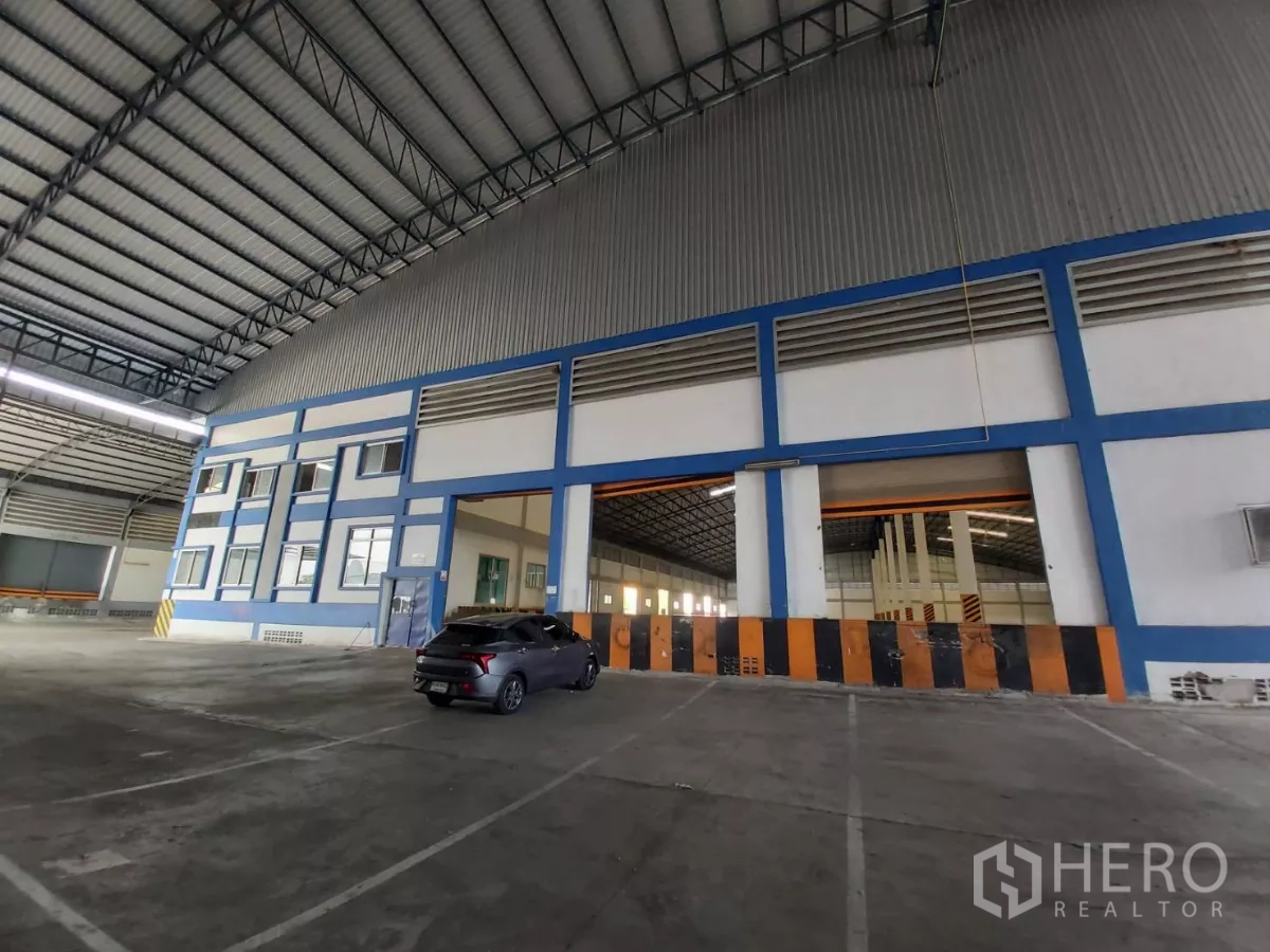 Warehouse for rent in Bang Bo, Samut Prakan - Multiple loading bays and office windows under a steel roof with a parked car.