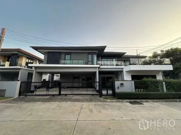 Detached House for sale in Lam Luk Ka, Pathum Thani - Modern two-storey detached house with wide balcony, gated driveway and evening sky in Lam Luk Ka.