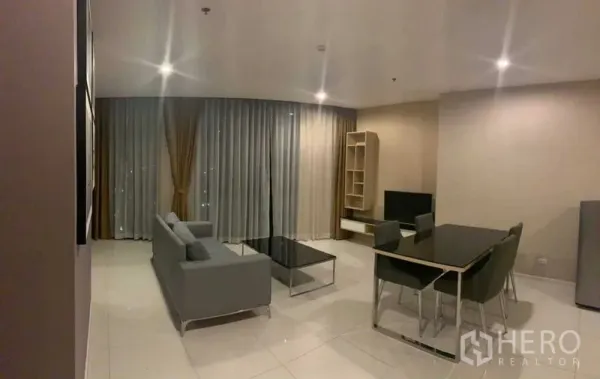 公寓 出租在Watthana, Bangkok - 夜景下的客厅，落地窗配长帘，沙发与餐桌，嵌灯照明。