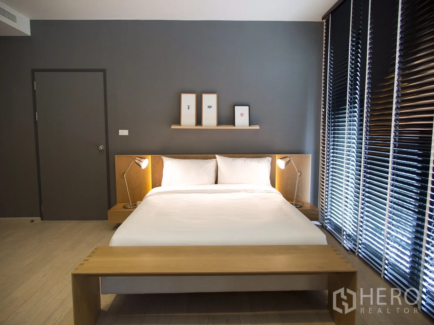 Condominium for rent in Watthana, Bangkok - Primary bedroom with king bed, wood bench, dark accent wall and large blinds.