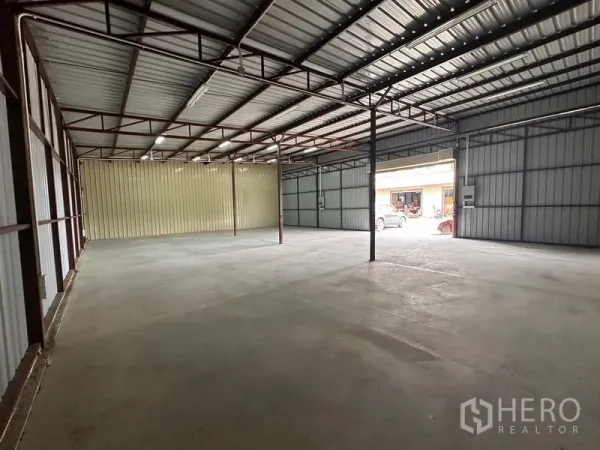 Warehouse for rent in Mueang Nonthaburi, Nonthaburi - Warehouse interior facing the loading bay with metal sheet walls, overhead lights, and vehicles visible outside.