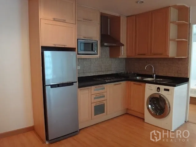 Condominium for rent in Bang Rak, Bangkok - Compact kitchen with wooden cabinets, black countertop, stainless fridge, microwave, range hood, and washing machine.