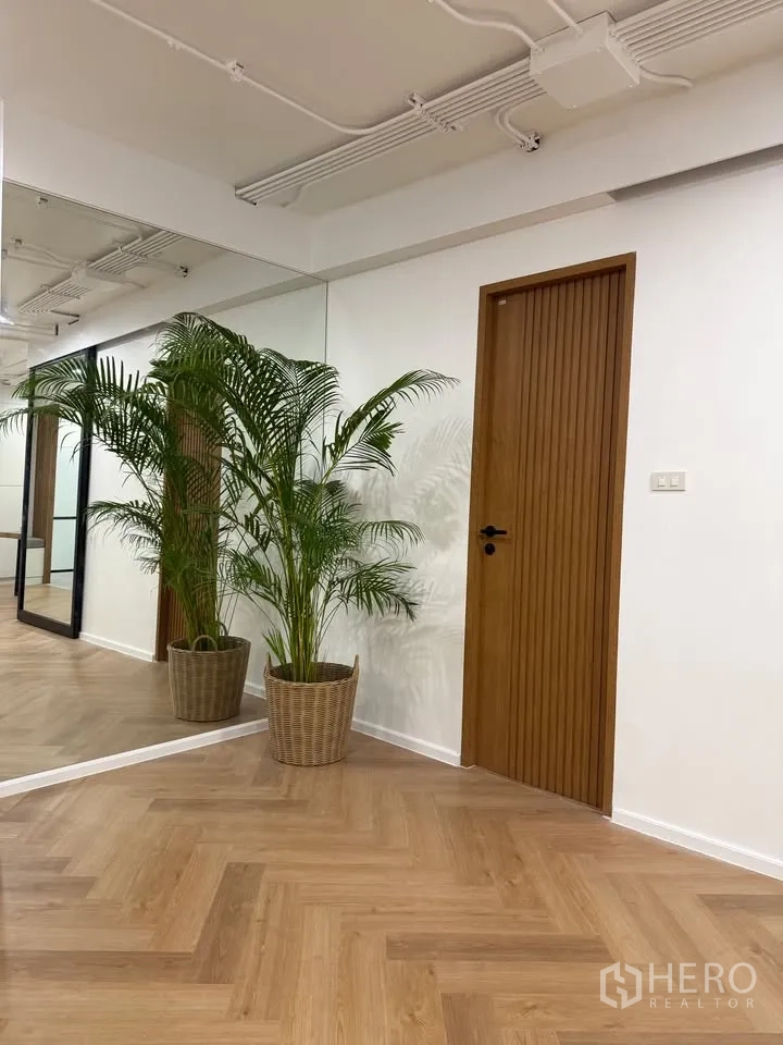 公寓 for rent in Watthana, Bangkok - 走廊设大镜面、木门与棕榈盆栽，人字形木地板。