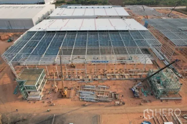Factory for rent in Bang Bo, Samut Prakan - Front aerial of an expansive warehouse steel structure with cranes, stacked materials, and two attached service buildings.