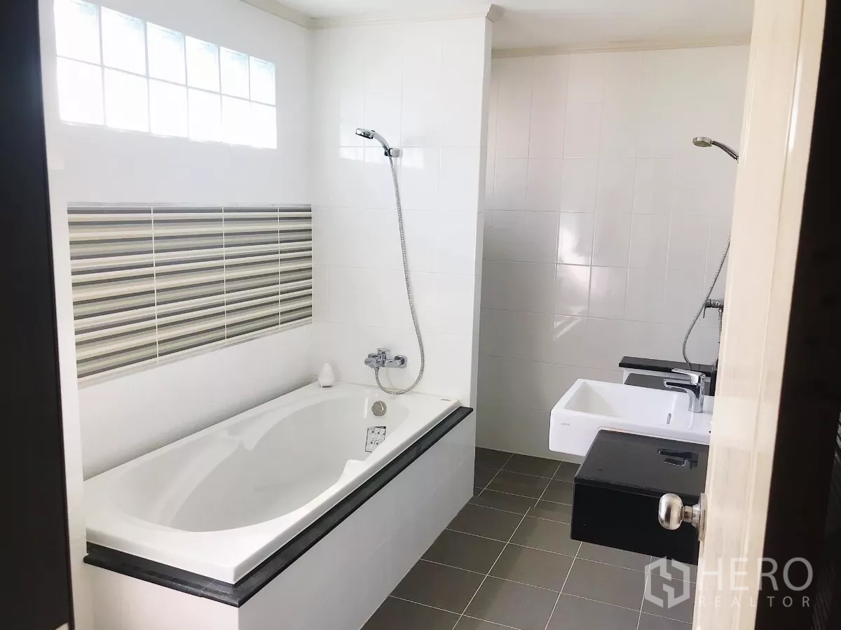 Detached House for sale in Lat Krabang, Bangkok - Family bathroom with bathtub, glass-block window and striped accent tiles.