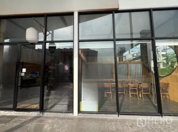 พื้นที่ขายปลีก ให้เช่าในWatthana, Bangkok - หน้าร้านกระจกสูง มองเห็นที่นั่งภายในและโคมแขวนเหนือทางเท้า.