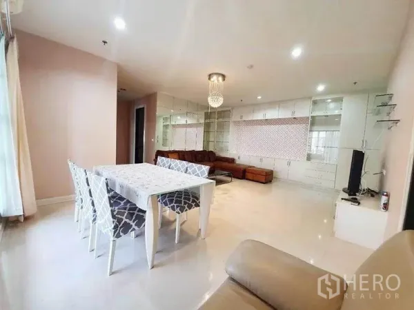 Condominium for rent in Ratchathewi, Bangkok - Open-plan lounge and dining with chandelier, white dining table, built-in cabinets and leather sectional.
