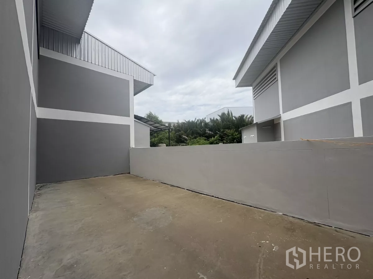 Factory for rent in Phra Samut Chedi, Samut Prakan - Rear service yard between buildings with concrete apron and low wall.